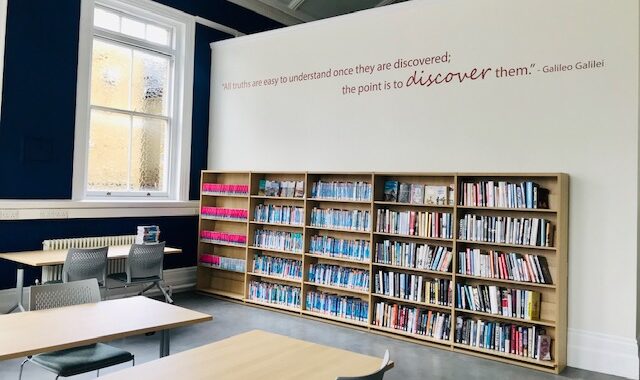 Twickenham Library's study area, showing desks, chairs and shelves of travel books. A quote on the wall above the shelves reads "All truths are easy to understand once they are discovered; the point is to discover them." - Galileo Galilei